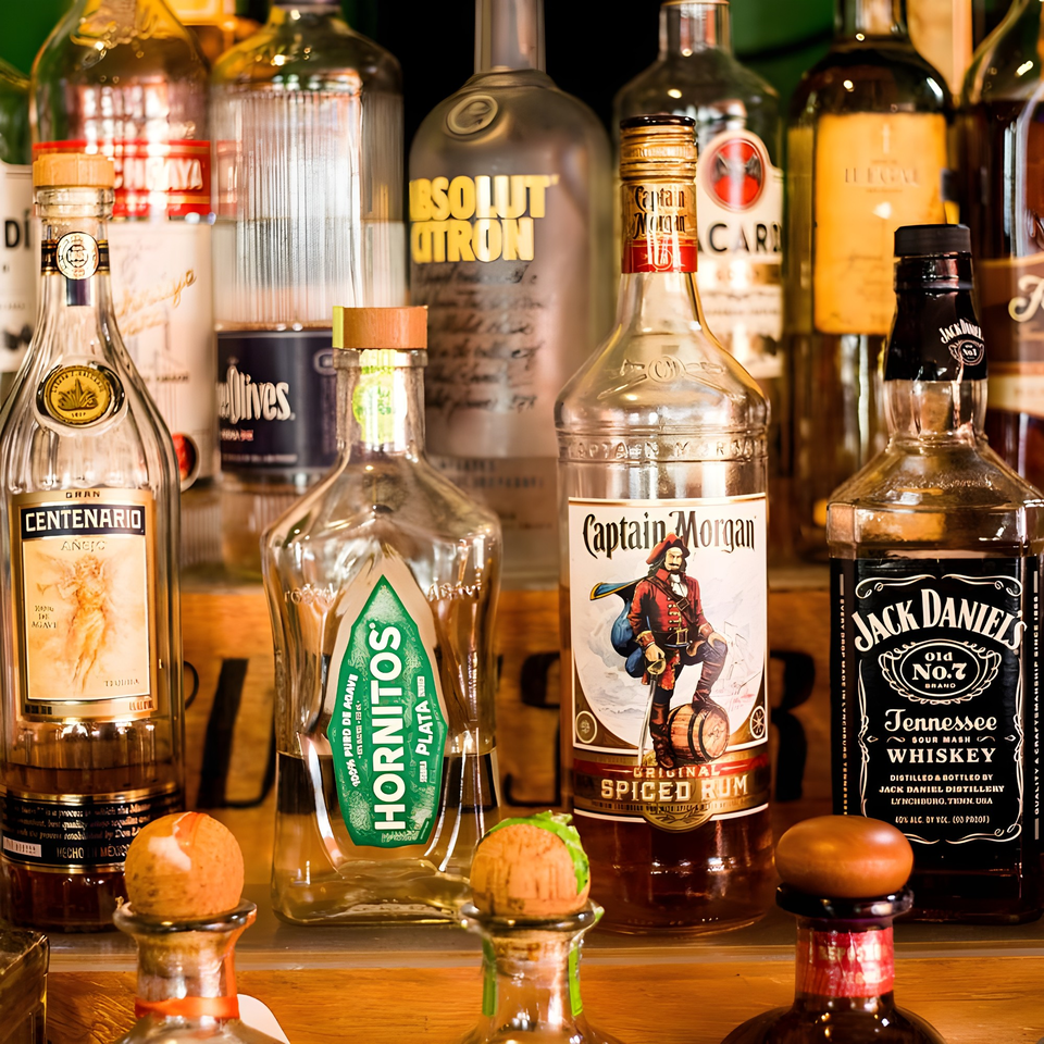 A collection of liquor bottles, including tequila, rum, and whiskey, displayed on a wooden shelf.