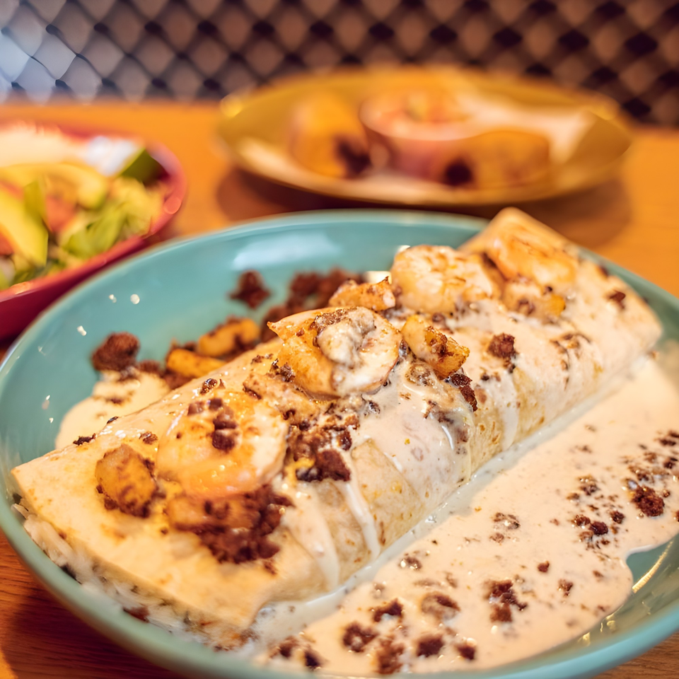 Shrimp burrito covered in white sauce and ground meat, served on a teal plate.